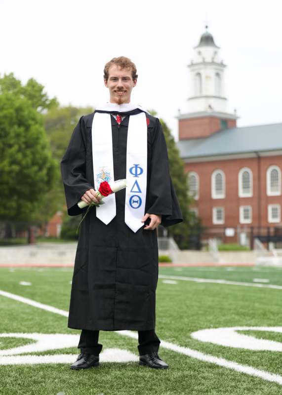 a man in a graduation gown holding a rose and a white sash