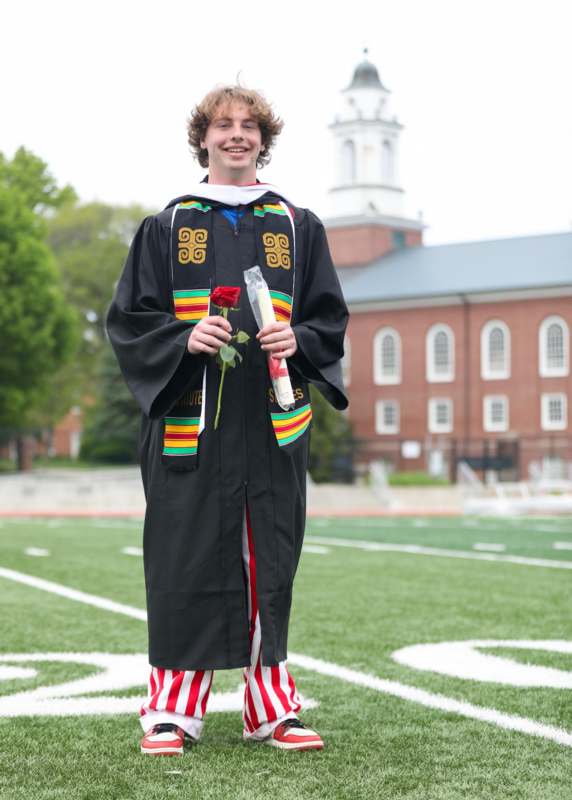 a man in a graduation gown holding a rose
