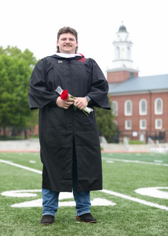 a man in a graduation gown holding a rose