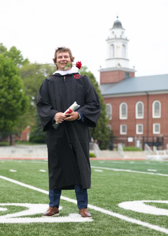 a man in a graduation gown holding a rose in his mouth