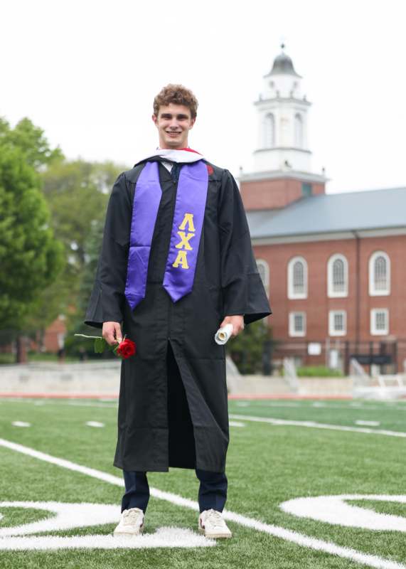 a man in a graduation gown holding a rose and diploma
