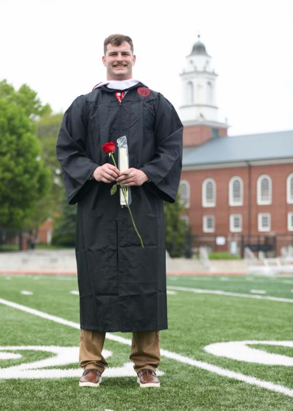 a man in a graduation gown holding a rose