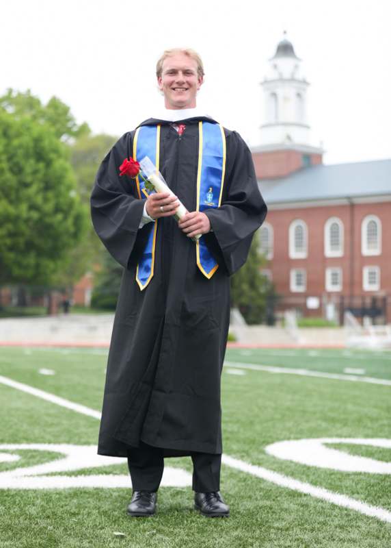 a man in a graduation gown holding a rose and a diploma