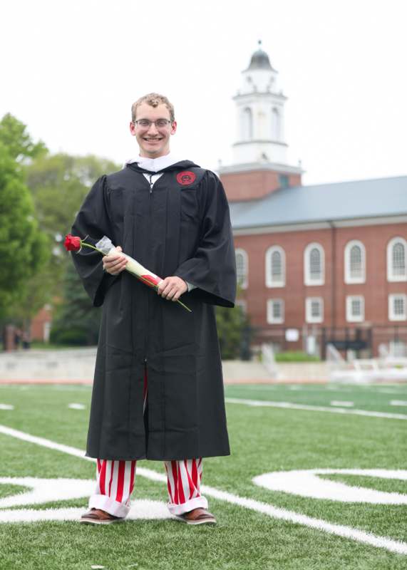 a man in a graduation gown holding a rose