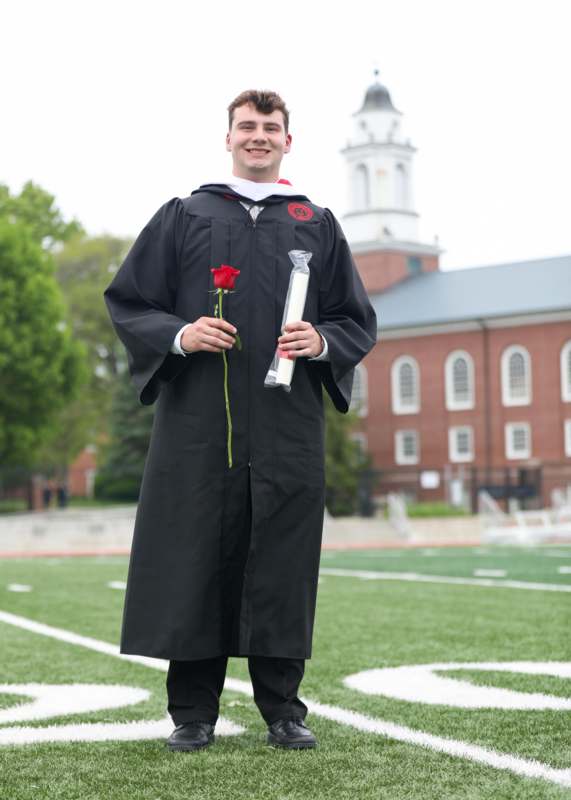 a man in a graduation gown holding a rose and a candle
