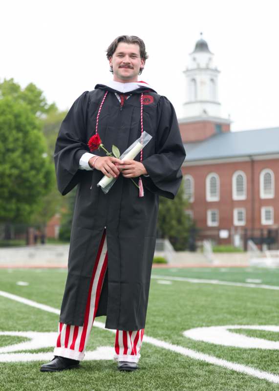 a man in a graduation gown holding a rose and diploma