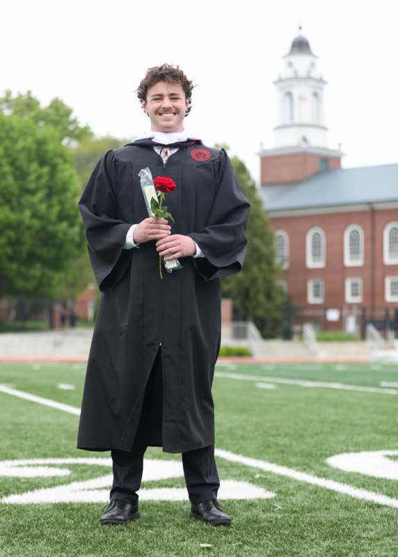 a man in a graduation gown holding a rose