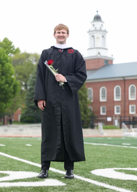 a man in a graduation gown holding a rose