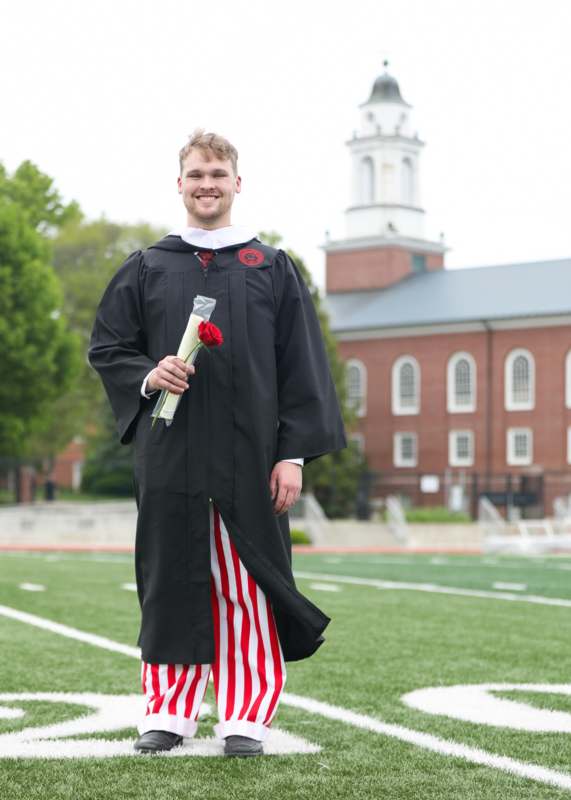 a man in a graduation gown holding a rose
