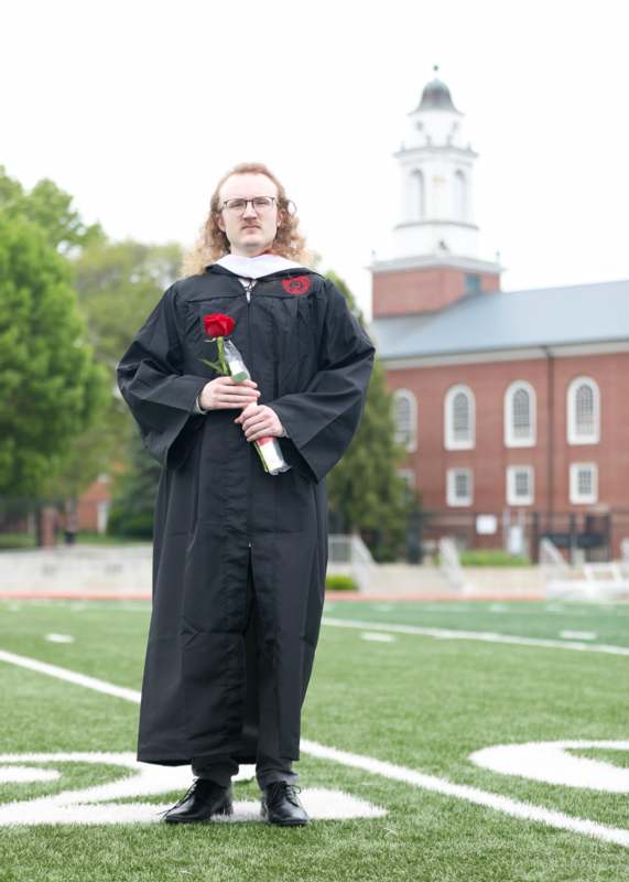 a man in a graduation gown holding a rose