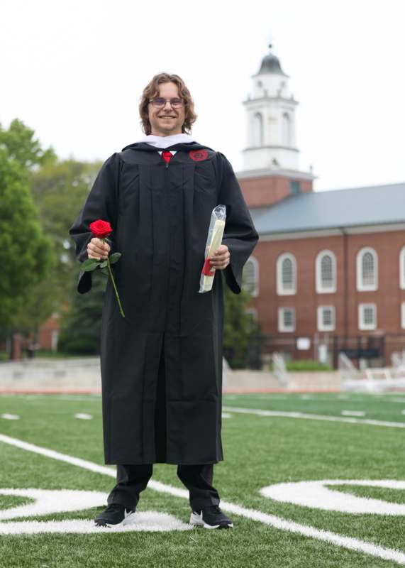 a man in a graduation gown holding a rose and a diploma
