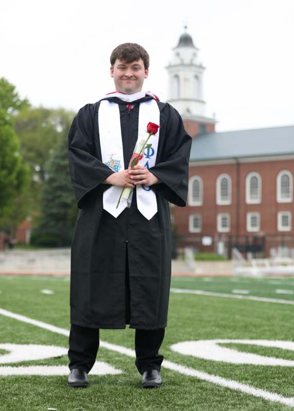 a man in a graduation gown holding a rose
