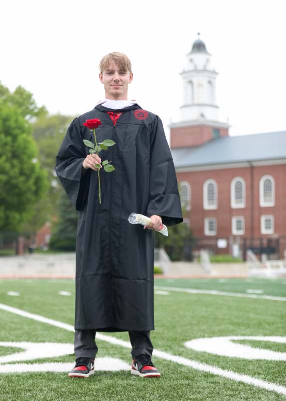 a man in a graduation gown holding a rose