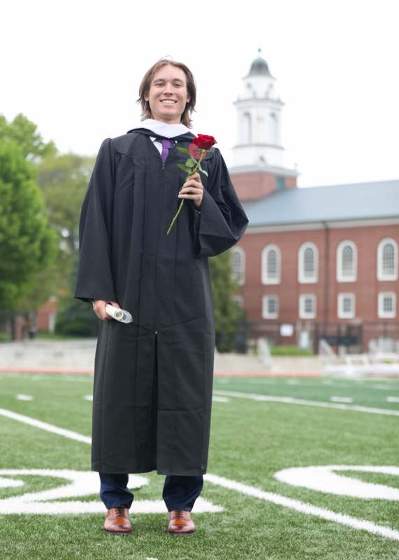 a man in a graduation gown holding a rose and a diploma