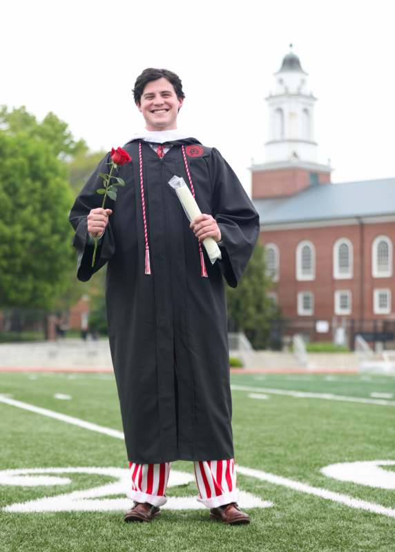a man in a graduation gown holding a rose and diploma