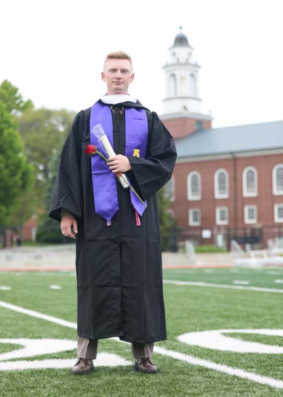 a man in a graduation gown holding a rose and a flower