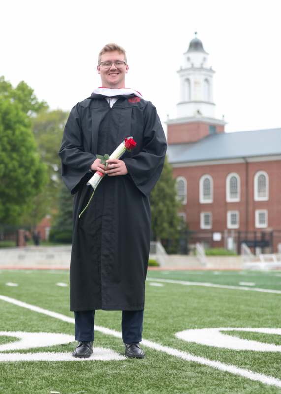 a man in a graduation gown holding a rose and standing on a football field