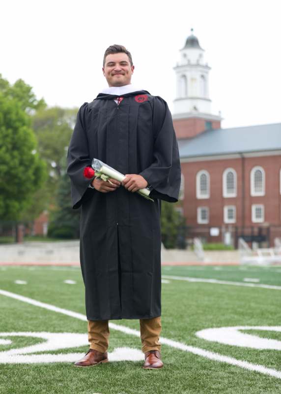 a man in a graduation gown holding a rose and a diploma