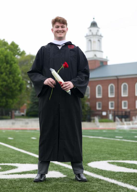 a man in a graduation gown holding a rose and a bottle