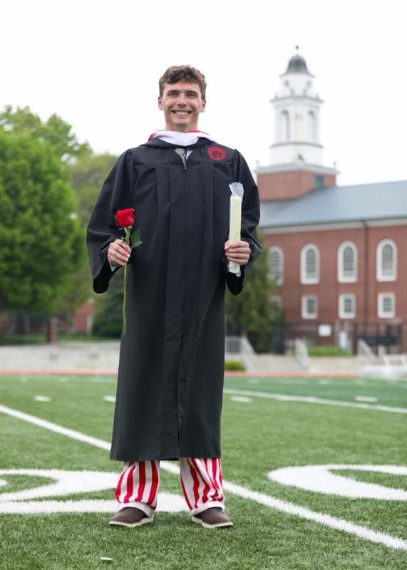 a man in a graduation gown holding a rose and candle