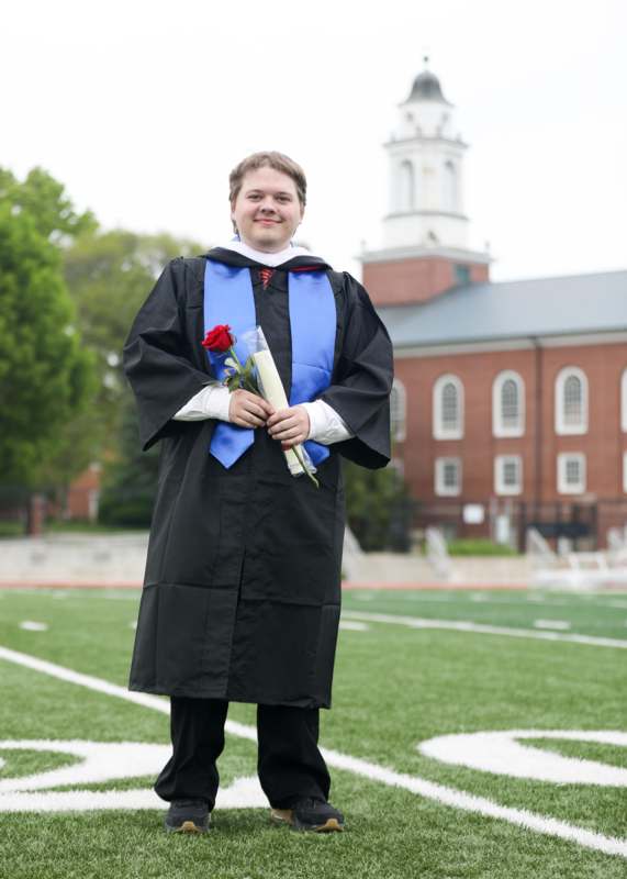 a man in a graduation gown holding a rose