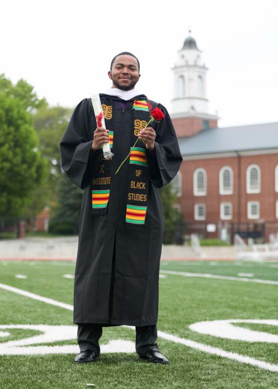 a man in a graduation gown holding a rose and a flower