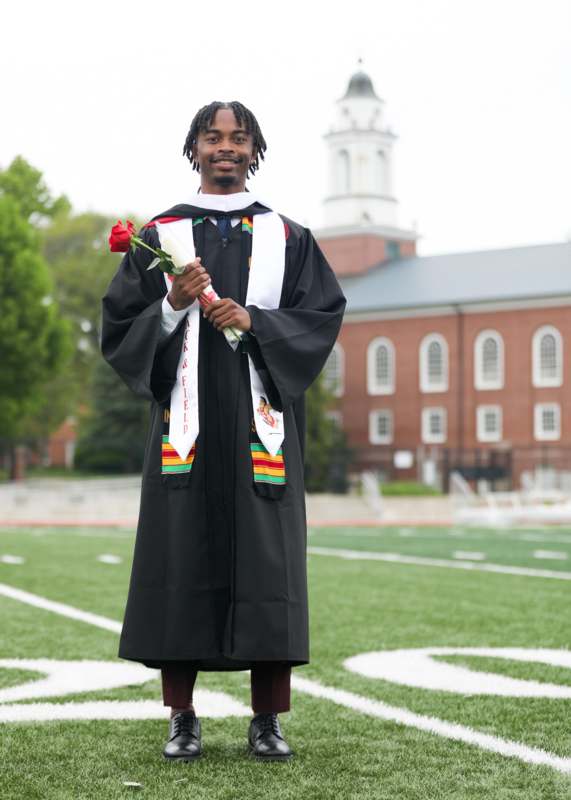 a man in a graduation gown holding a rose