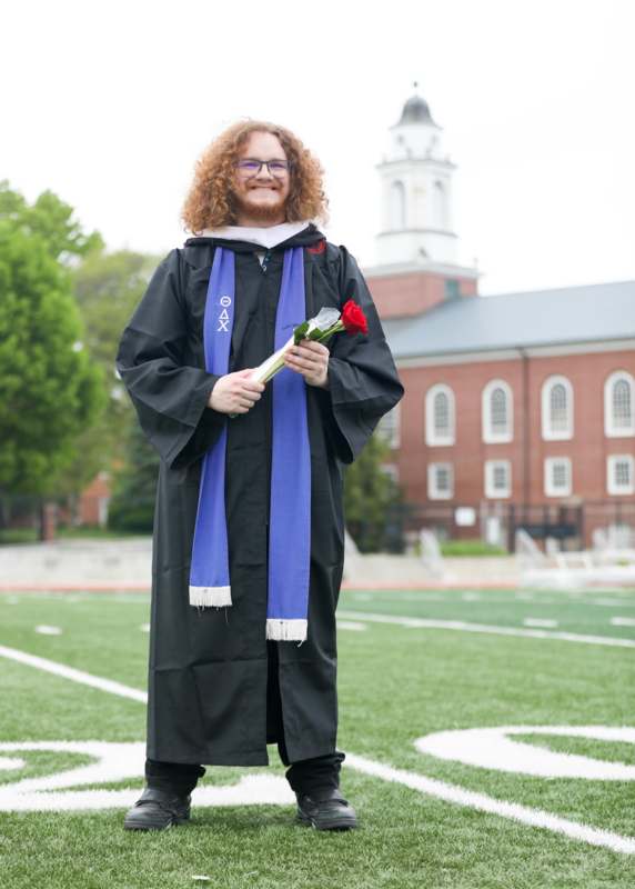 a man in a graduation gown holding a rose and a blue scarf