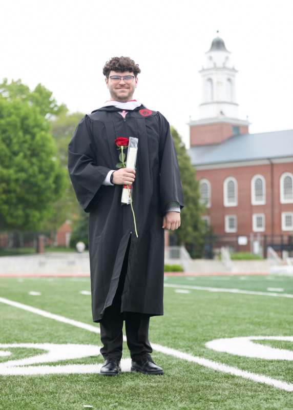 a man in a graduation gown holding a rose