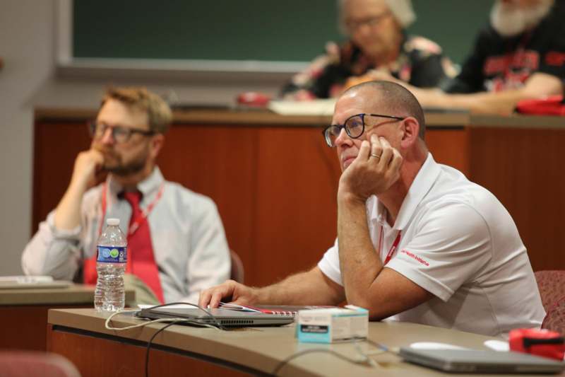 a man in glasses sitting at a table with a laptop and a bottle of water