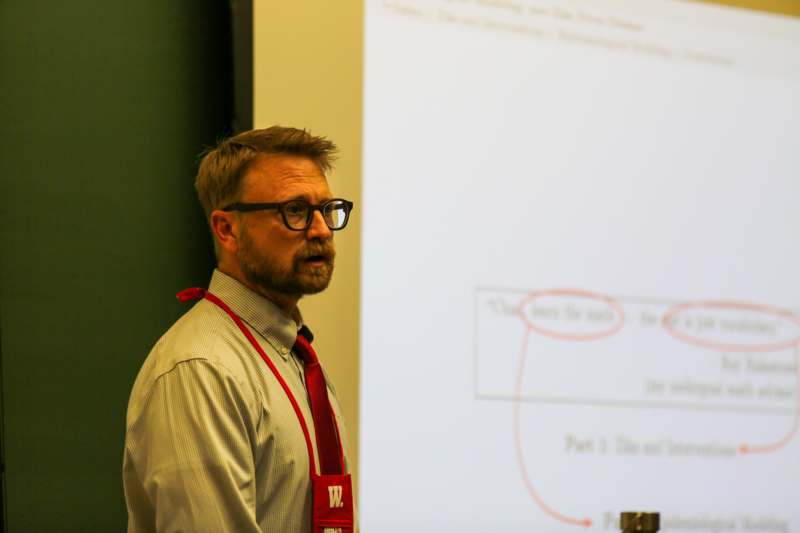 a man in glasses and a red tie standing in front of a projection screen