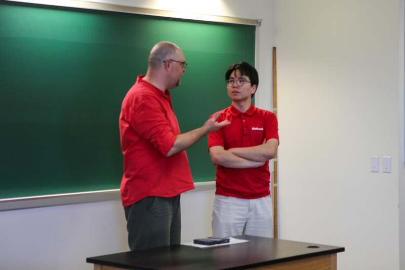 a man in red shirt standing in front of a chalkboard