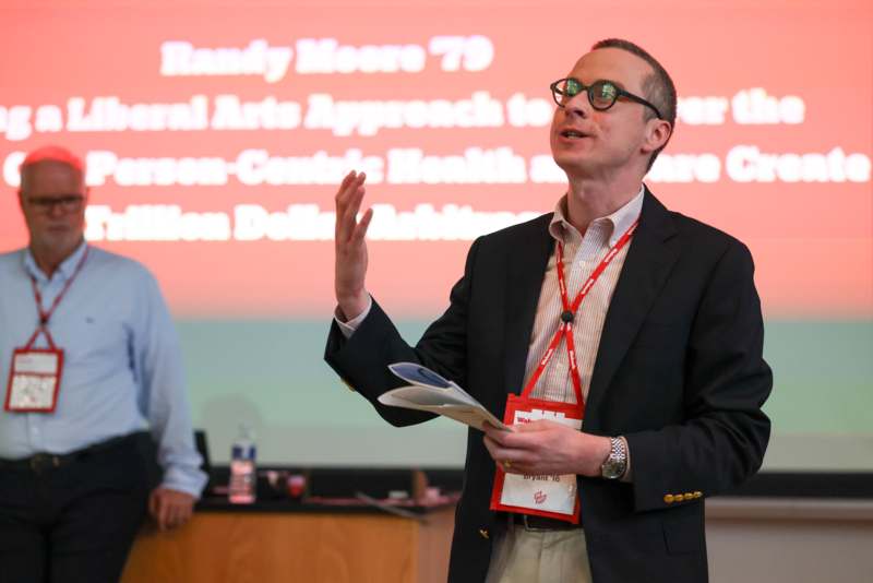 a man in a suit and glasses standing in front of a screen