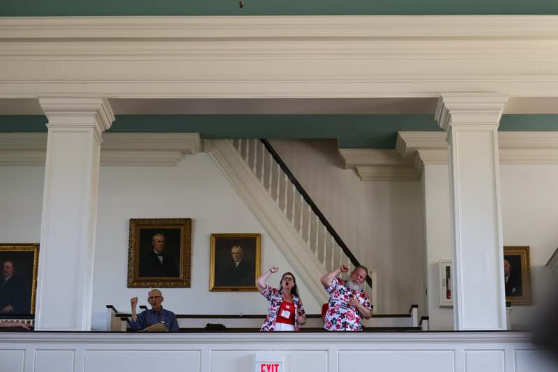 a group of people standing in a room with a white wall and a staircase