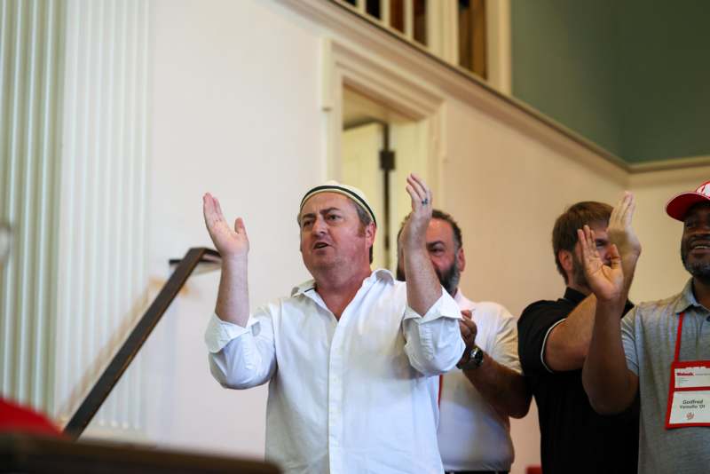 a group of men standing in a room with a staircase and a white wall