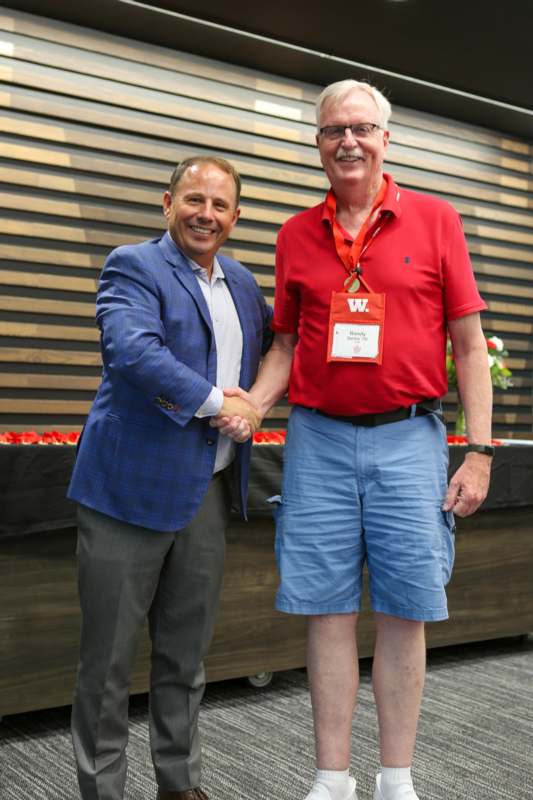 two men shaking hands in front of a wood wall