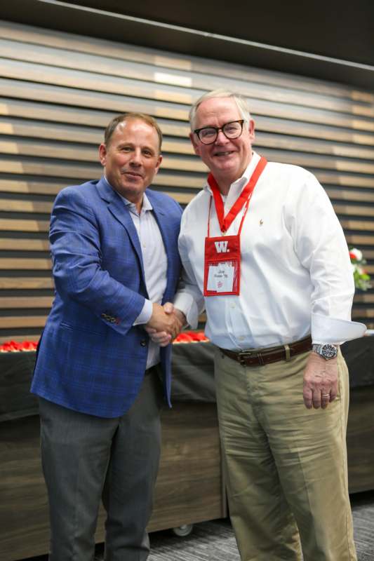 two men shaking hands in front of a wood wall