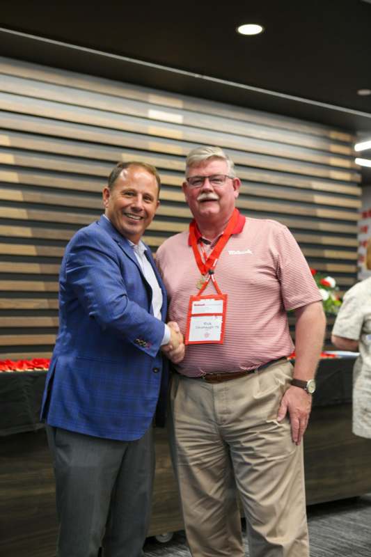 two men shaking hands in front of a wood wall