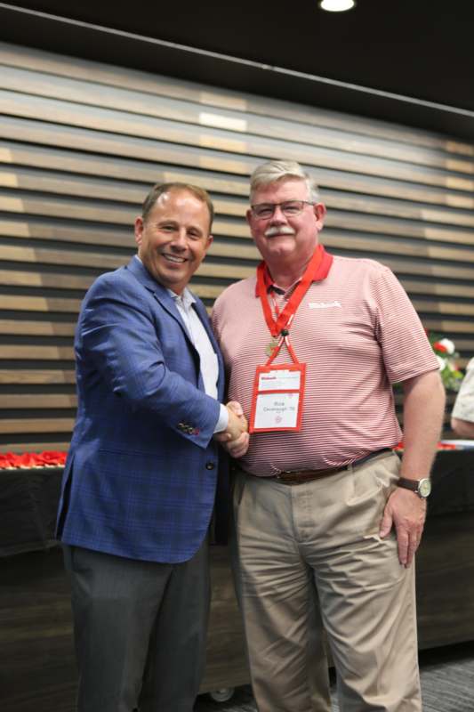 two men shaking hands in front of a wood wall