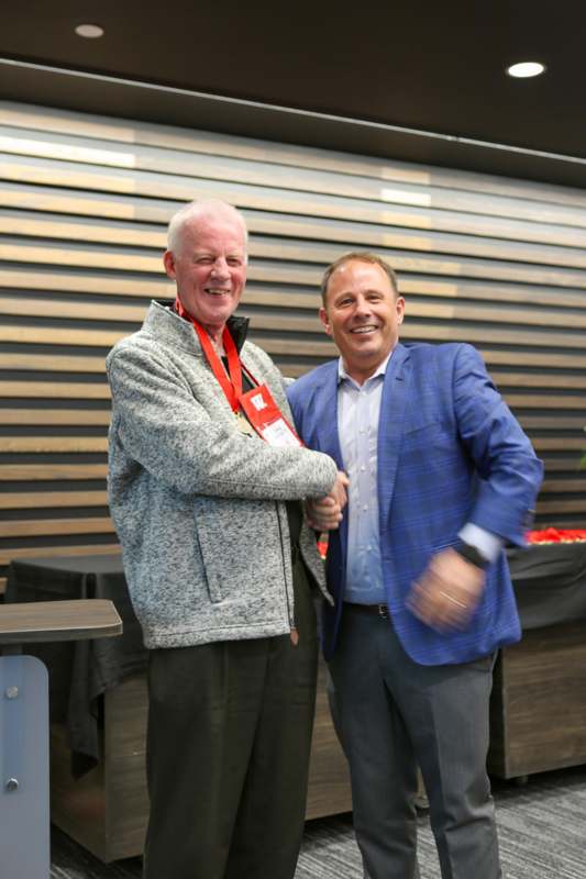 two men shaking hands in front of a wood wall