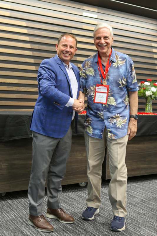 two men shaking hands in front of a wood wall