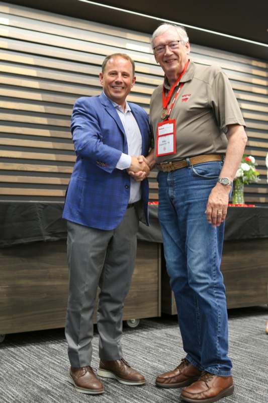two men shaking hands in front of a wood wall