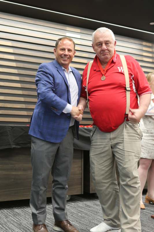 two men shaking hands in front of a wood wall