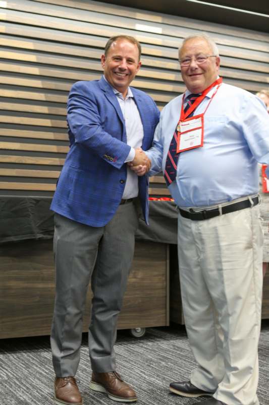 two men shaking hands in front of a wood wall