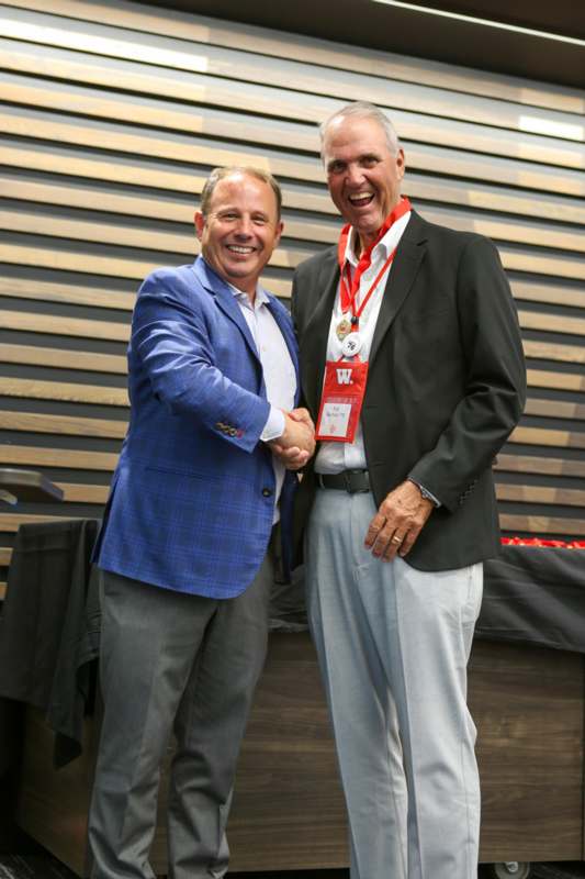 two men shaking hands in front of a wood wall