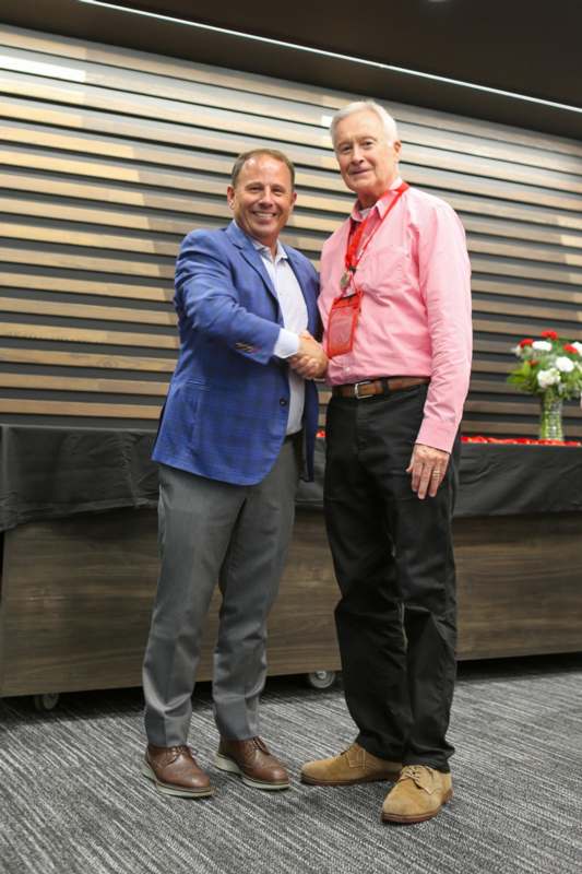 two men shaking hands in front of a wood wall