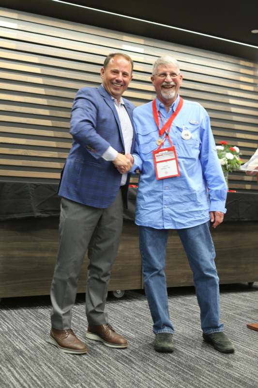 two men shaking hands in front of a wood wall