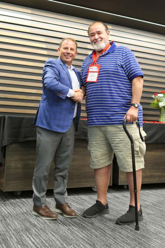two men shaking hands in front of a wood wall