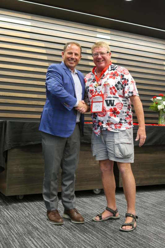 two men shaking hands in front of a wood wall