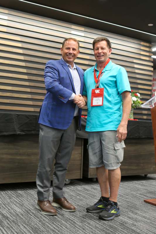 two men shaking hands in front of a wood wall